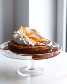 a cake with whipped cream and caramel on top sits on a glass platter