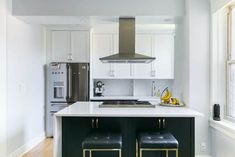 a kitchen with two stools next to an oven and refrigerator in the middle of it