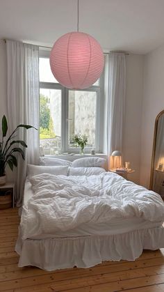 a white bed sitting under a pink light in a bedroom next to a large window