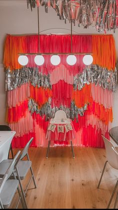 an orange and red curtain is hanging over a table with white chairs in front of it