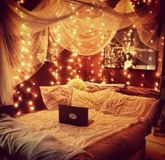 a laptop computer sitting on top of a bed covered in fairy lights and drapes