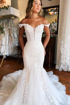 a woman wearing a white wedding dress standing in front of a mirror with her hands on her hips