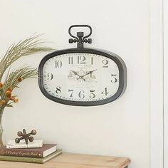 a clock is hanging on the wall above a table with flowers and books next to it