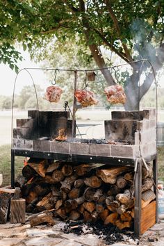 an outdoor bbq grill with meat on it and wood stacked in front of it