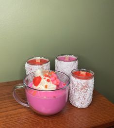 four candles are sitting in a bowl on a table next to two cups with candy and marshmallows