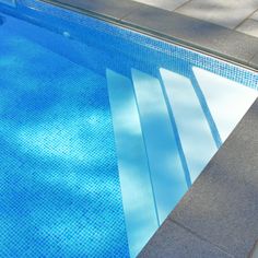 an empty swimming pool with blue water and tile flooring on the side, next to a sidewalk