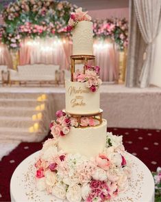 a three tiered wedding cake with pink and white flowers on the top, sitting on a table