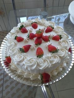 a cake with white frosting and strawberries on top sitting on a glass table