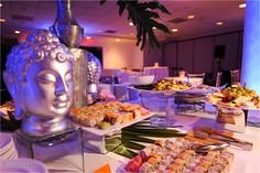 a buffet table filled with different types of food and desserts on trays next to a buddha statue