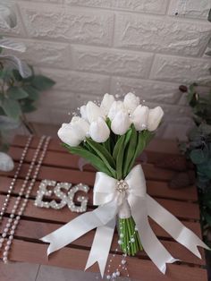 a bouquet of white tulips tied to a ribbon on a wooden table with pearls