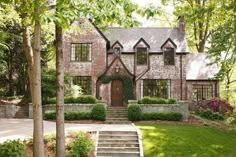 a large brick house surrounded by lush green trees and shrubbery with stairs leading up to the front door