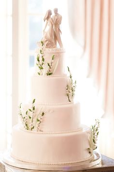 a three tiered wedding cake with an angel figurine on top and flowers