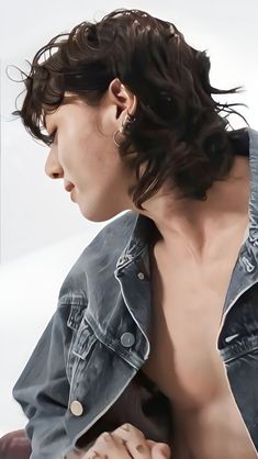 a close up of a person wearing a jean jacket and earring on their left side