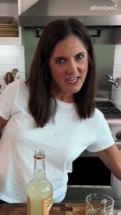 a woman standing in front of a bottle of alcohol on top of a wooden counter