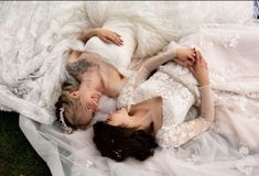 two women laying on top of each other in white wedding gowns and veils