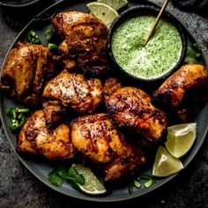 grilled chicken on a plate with green sauce and garnished with limes