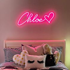 a pink neon sign above a bed with pillows