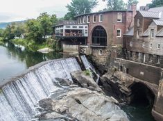 people are standing at the top of a waterfall in front of some buildings and a body of water