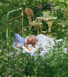 an older man sleeping in the middle of a garden with lots of flowers and plants