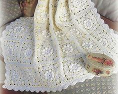 a crocheted baby blanket is laying on a bed with an infant doll in it