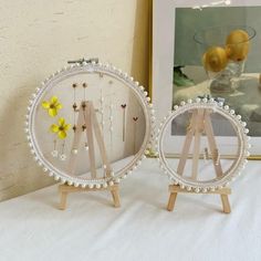 two white beaded pictures on wooden easels next to a vase with yellow flowers