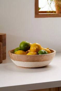 a wooden bowl filled with lemons and limes on top of a white counter