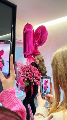 a woman taking a selfie with her cell phone while holding pink flowers and balloons