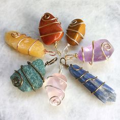 seven different colored stone pendants sitting on top of a white surface with wire wrapped around them