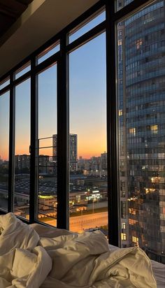 an unmade bed in front of large windows overlooking the city at sunset or dawn