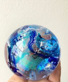 a hand holding a glass ball with blue and white designs on it's surface