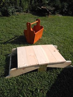 a wooden bench sitting on top of a lush green grass covered field next to an orange chair