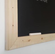 a chalkboard with some writing on it in front of a white wall and wooden frame