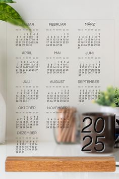 a desk with a calendar on it next to a potted plant and glass vase