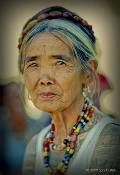 an old woman with tattoos on her face and neck is looking at the camera while wearing beads