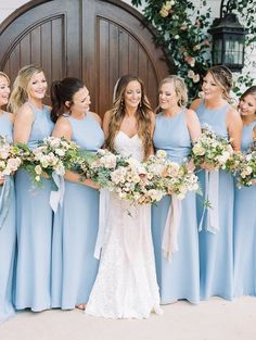 a group of women standing next to each other in front of a wooden door holding bouquets