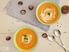 two bowls of carrot soup on a table with spoons and nuts next to it