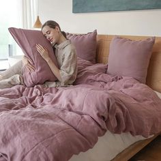 a woman is laying in bed with her arms around the pillow while reading a book