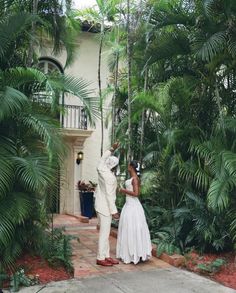 a bride and groom standing in front of a house surrounded by palm trees on their wedding day