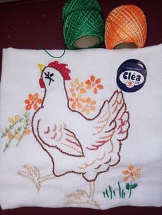 a close up of a piece of cloth with a chicken on it and two balls of yarn in the background