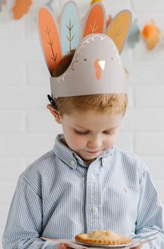 a young boy wearing a paper turkey hat holding a plate with a pastry on it