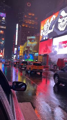 cars are driving down the street in the rain at night, with neon lights and billboards behind them