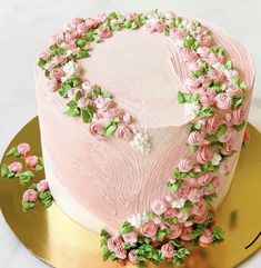 a heart shaped cake with pink frosting and flowers around it on a gold platter