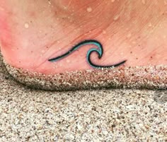 a foot with a small wave tattoo on it's side, and sand around it