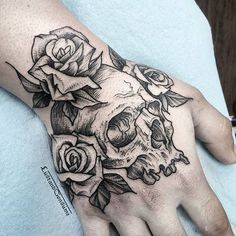 a hand with a skull and roses tattoo on it