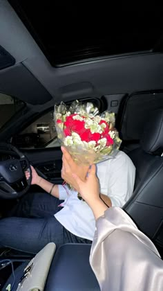 a woman sitting in the driver's seat of a car holding a bouquet of flowers