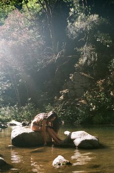 a woman is sitting on rocks in the water