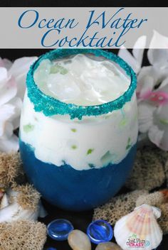 an ocean water cocktail with blue and green sprinkles on the rim, surrounded by seashells