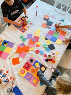 two children are sitting at a table making colorful paper shapes with crayons and markers