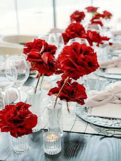 red flowers are in vases on a table with wine glasses and napkins around it