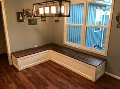 an empty room with a window and bench in the corner, next to a wooden floor